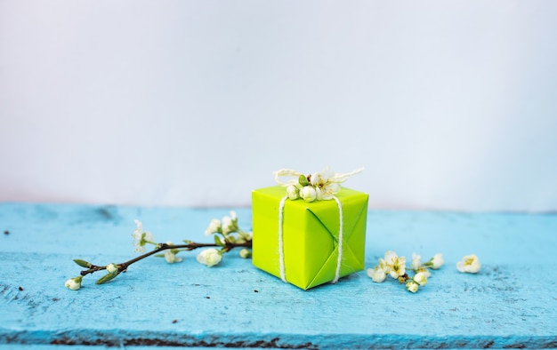 Geschenkbox der hellgrünen Farbe auf einem blauen Frühlingshintergrund, Frühlingsblumen. Frühlingszusammensetzung.