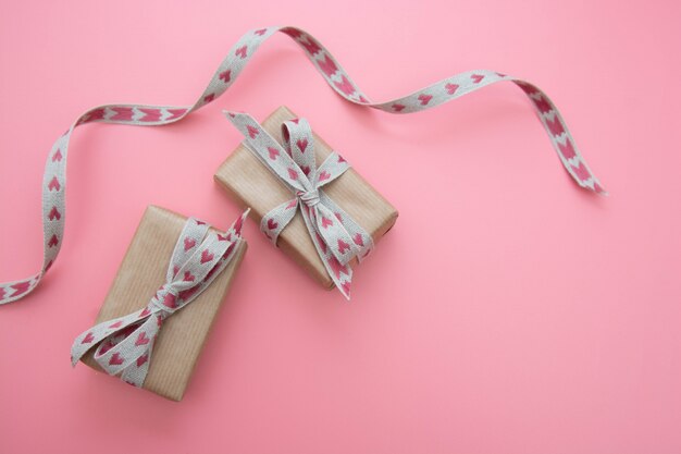 Geschenkbox eingewickelt in Kraftpapier und Bogen, auf Rosa. Valentinstag, Geburtstag.