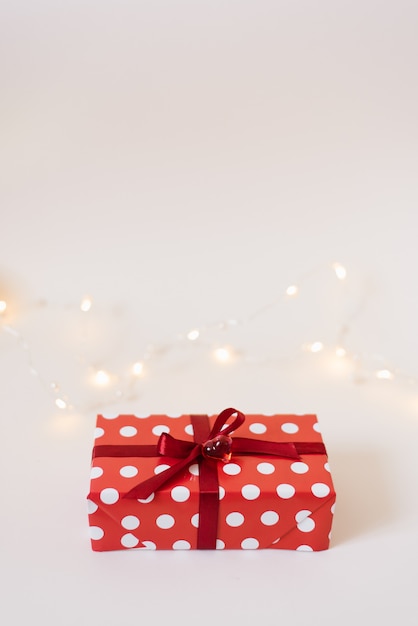 Geschenkbox in der roten Papierverpackung mit den weißen Tupfen, gebunden mit einem roten Satinband mit einem Bogen und einem Glasherzen auf Weiß