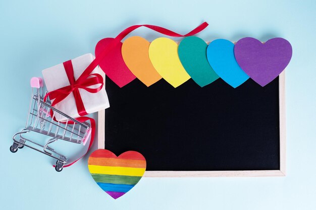 Geschenkbox in Einkaufswagen mehrfarbige regenbogenfarbene Papierherzen und ein leeres Brett mit Kopierraum