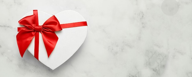 Geschenkbox in Form eines Herzens mit einer roten Schleife auf einem weißen Tisch.