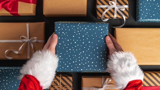 Foto geschenkbox in santa claus-händen und weihnachtsdekorationen auf schwarzem tisch hautnah