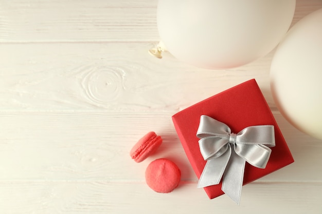 Geschenkbox, Luftballons und Makronen auf weißem Holztisch