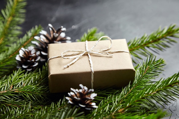 Geschenkbox mit grünen Weihnachtsbaumzweigen und Zapfen auf dunklem Hintergrund