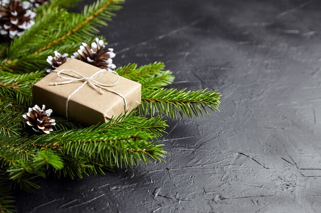 Geschenkbox mit grünen Weihnachtsbaumzweigen und Zapfen auf dunklem Hintergrund