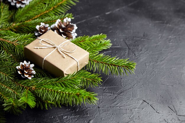 Geschenkbox mit grünen Weihnachtsbaumzweigen und Zapfen auf dunklem Hintergrund