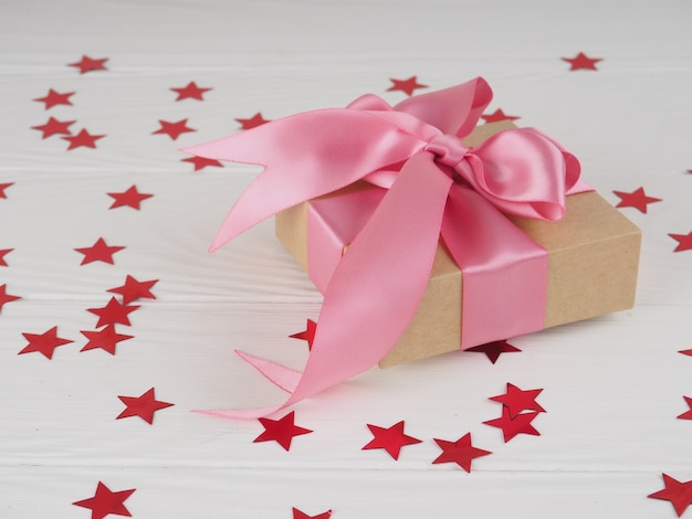 Geschenkbox mit hellem rotem rosa Band auf weißem Hintergrund mit Sternen