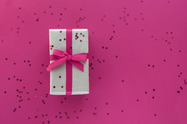 Geschenkbox mit rosa Band und Konfetti-Dekorationen auf buntem Hintergrund des Pastellpapiers. Flache Lage, Draufsicht, Kopierraum