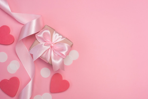 Geschenkbox mit rosa Schleife auf pastellrosa Tisch mit weißem Konfetti und Herzen