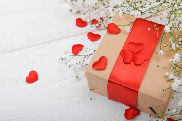 Geschenkbox mit roten Herzen auf einem weißen Hintergrund mit kleinen weißen Blumen, Feier Valentinstag