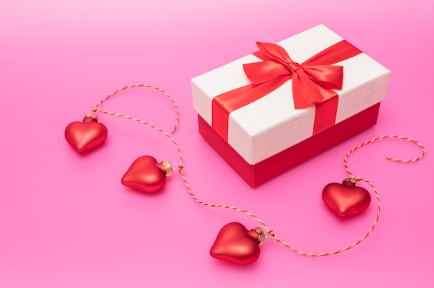 Geschenkbox mit Schleife und herzförmiger Dekoration auf rosa Hintergrund als Konzept für Valentinstag