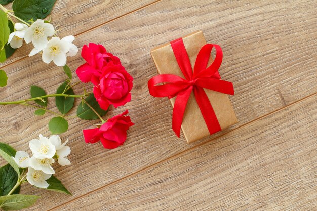 Geschenkbox mit schönen Rosen- und Jasminblüten auf dem Holzhintergrund. Konzept, an Feiertagen ein Geschenk zu machen. Ansicht von oben.