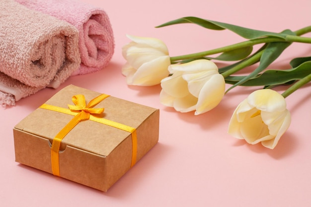 Geschenkbox mit schönen Tulpen und Handtuch auf rosa Hintergrund Konzept, an Feiertagen ein Geschenk zu machen