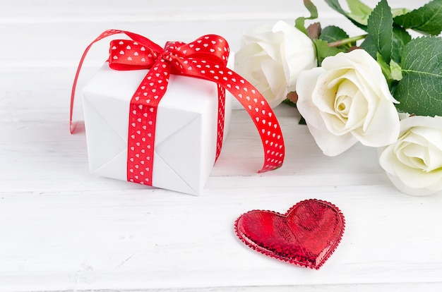 Geschenkbox mit Strauß weißer Rose auf weißem Holztisch.