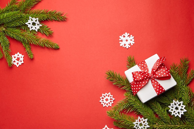 Geschenkbox mit Weihnachtsbaumast und weißen Schneeflocken auf rotem Hintergrund Draufsicht