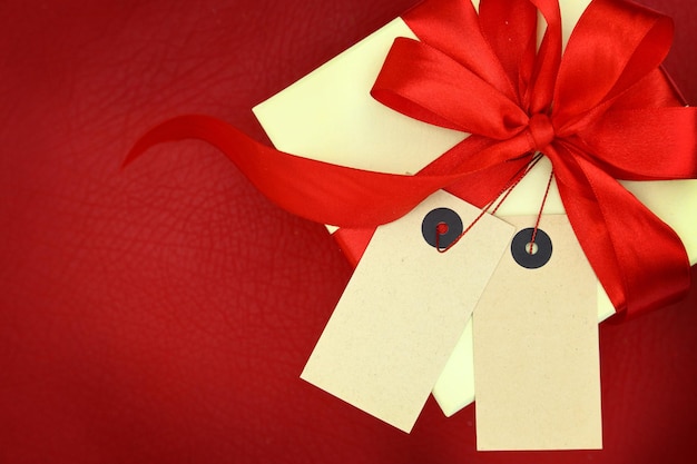 Geschenkbox mit zwei leeren Tags und Farbband auf rotem Hintergrund
