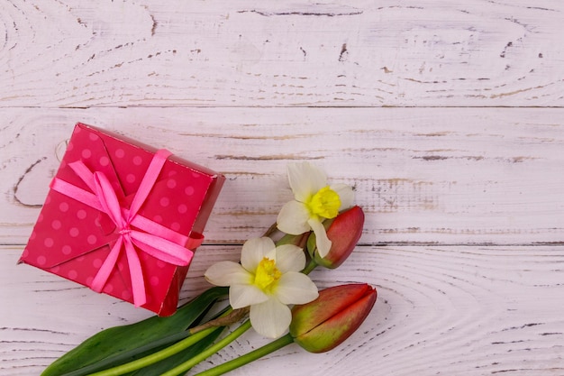 Geschenkbox und Blumenstrauß aus roten Tulpen und Narzissen auf weißem Holzhintergrund Konzept des Valentinstags Frauentag Muttertag und Geburtstag Draufsicht Kopierraum