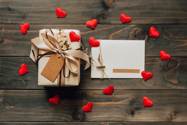 Geschenkbox und Grußkarte mit Bogenband und Papierherzen auf Holztisch zum Valentinstag. Platz kopieren.