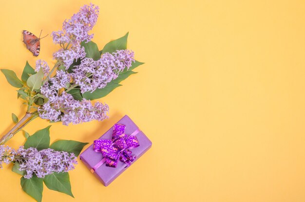 Geschenkbox und lila Blumen auf gelbem Grund mit Kopienraum