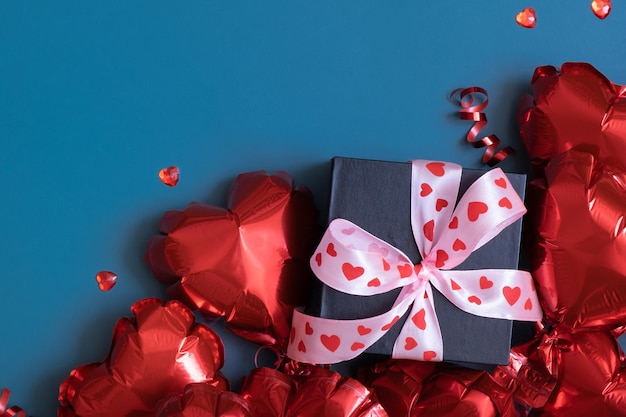 Geschenkbox und rote herzförmige Luftballons auf blauem Hintergrund Valentinstag flach Zusammensetzung