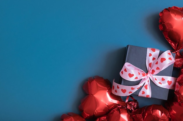 Geschenkbox und rote herzförmige Luftballons auf blauem Hintergrund Valentinstag-Grußkarte Platz kopieren