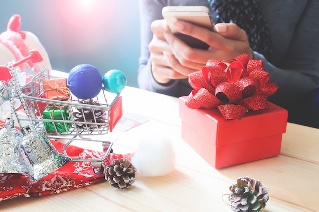 Geschenkbox und Weihnachtsverzierung auf Tabelle mit der Frau, die Handy verwendet