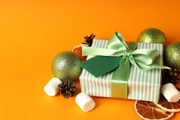 Geschenkbox und Weihnachtszubehör auf orangem Hintergrund.