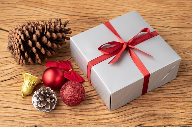 Geschenkbox, Weihnachtskugeln und Bogen über Holztisch.