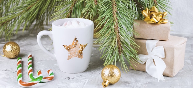 Geschenkboxen, heißes Getränk mit Marshmallows, Zuckerstangen und goldenen Kugeln auf schäbigem Grau