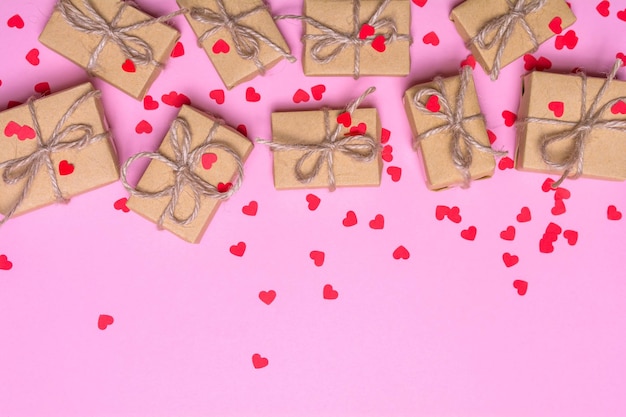 Geschenkboxen in Kraftpapier auf rosafarbenem Hintergrund Konfetti-Herzen und Goldbänder