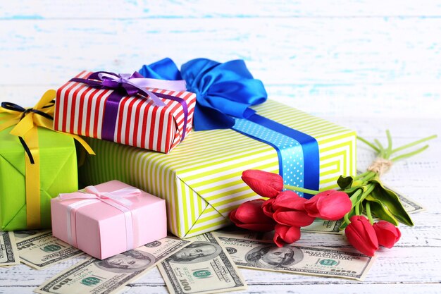 Geschenkboxen mit Geld und Blumen auf farbigem Holzhintergrund