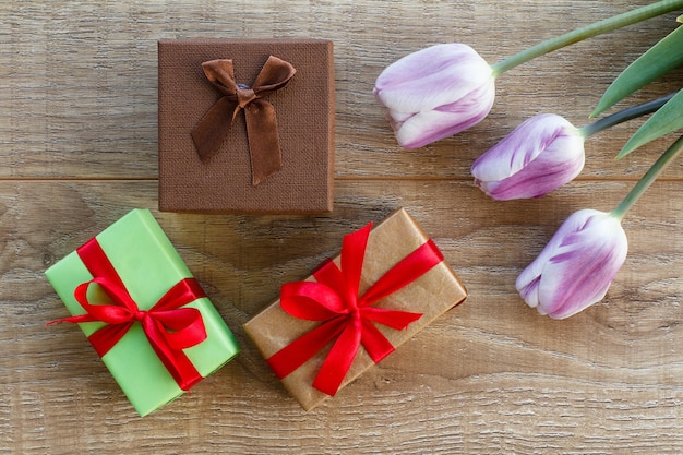 Geschenkboxen mit roten Bändern und schönen Tulpen auf den Holzbrettern Ansicht von oben