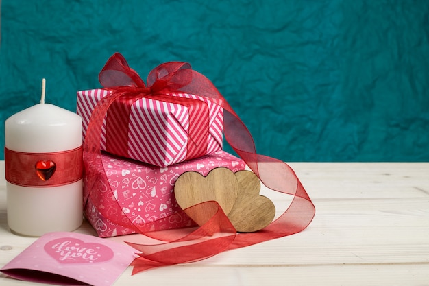 Geschenkboxenszene mit Kerze, Herzen und Grußkarte auf hellem Holz und türkisfarbenem Hintergrund