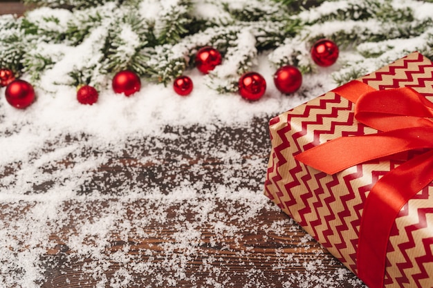 Geschenke auf hölzernem Hintergrund mit den Tannenbaumasten und rotem Flitter pulverisierten mit Schnee