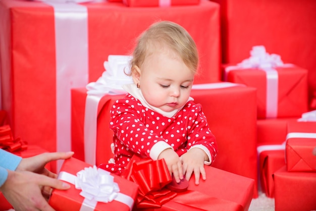 Geschenke für das erste Weihnachten des Kindes. Feiern Sie das erste Weihnachten. Teilen Sie die Freude über das erste Weihnachten des Babys mit der Familie. Das erste Weihnachten des Babys, ein einmaliges Ereignis im Leben. Kleines Mädchen spielt in der Nähe eines Stapels von Geschenkboxen