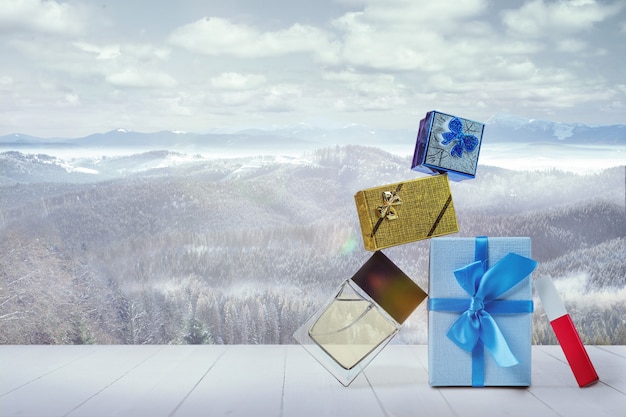 Geschenke für Familie oder Freunde und Berglandschaft im Hintergrund. Kisten und Parfums vor schneebedeckten Bergen und bewölktem Himmel. Wintertag, Feiertage, Reisen, Neujahr und Weihnachtszeit. .