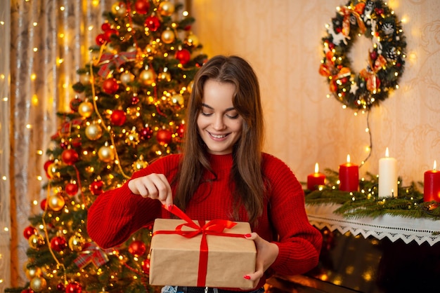 Geschenke für Weihnachten Neujahrsfeier Fröhliches Mädchen, das Weihnachtsgeschenk in einem dekorierten Raum öffnet, freut sich, ein Geschenk von einem geliebten Menschen zu erhalten