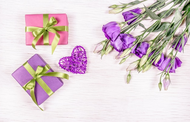 Geschenke und Blumen. Boxen mit Geschenken und einem Blumenstrauß Eustoma auf einem weißen Hintergrund. Weidenherz. Romantisches Konzept.