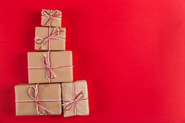 Geschenke vom Kraftpapier und von den Weihnachtsbaum-förmigen Seilen auf einem Rot, Weihnachten, Grußkarte copyspace.