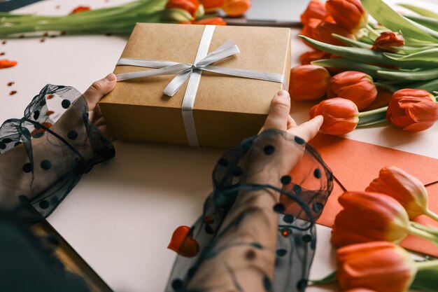 Foto geschenkkiste mit einem bogen und tulpen in den händen eines mädchens festlicher hintergrund