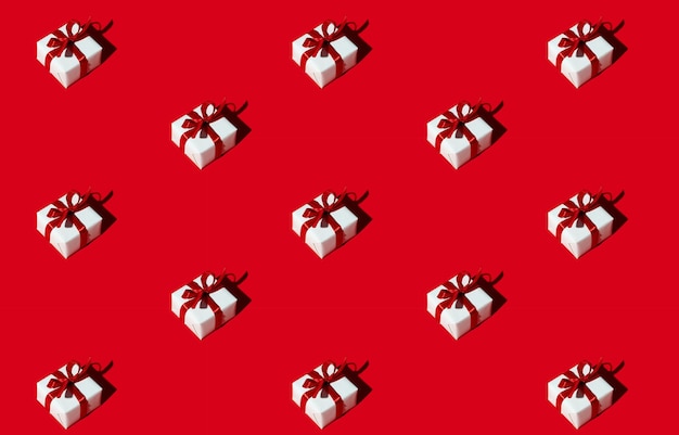 Geschenkmuster. Roter nahtloser Hintergrund. Valentinstag. Romantische Überraschung. Minimalistische diagonale Komposition von Geschenken in weißen Schachteln mit Schleifen einzeln auf hell.