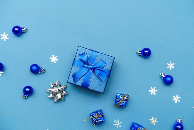 Geschenkpapierbox-Banner mit blauer Schleife und dunkelblauen Weihnachtskugeln auf blauem Hintergrund mit Schn...