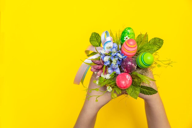 Geschenkstrauß zu Ostern. Handgemachter Blumenstrauß mit dekorativen Ostereiern und Blumen in den Händen eines Kindes. Kind, das einen Blumenstrauß in seinen Händen auf einem gelben Hintergrund hält.