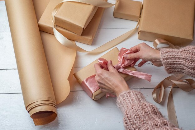 Geschenkverpackung in Kraftpapier Geschenkverpackung in Kraftpapier Frauenhände verpacken Schachteln mit Geschenken und Schleifen aus hellem Band