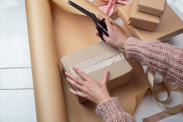 Geschenkverpackung in Kraftpapier Geschenkverpackung in Kraftpapier Frauenhände verpacken Schachteln mit Geschenken und Schleifen aus hellem Band