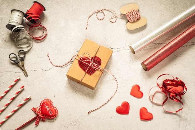 Geschenkverpackungszubehör zum Valentinstag und Geschenkbox mit Paillettenherz auf grauem Steinhintergrund