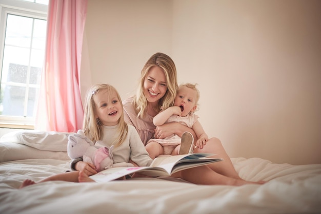 Geschichten sind ein Spaß für die ganze Familie Aufnahme einer entzückenden dreiköpfigen Familie, die zusammen ein Buch zu Hause auf dem Bett liest