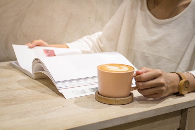 Geschlossen herauf die Hände, die Tasse latte Kunstkaffee halten und Zeitschrift oder Buch öffnen.