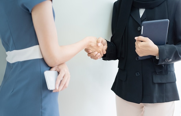 Geschlossene hand betrügt von zwei frauen eine in muslimischen hijab hand halten tablette ein kleid in modernen anzug hand halten smartphone, erfolg geschäftskonzept.