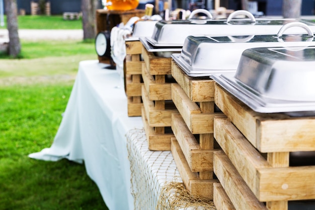 Geschlossene Speisenwärmer aus Edelstahl auf weißer Tischdecke am Catering-Tisch vor einer Party im Freien in einem Hotelgarten Horizontales Foto